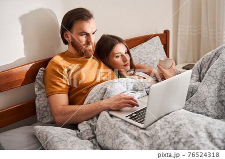 Cheerful couple using laptop and hugging while lying on bed Cheerful couple using laptop and hugging while lying on bed 76524318