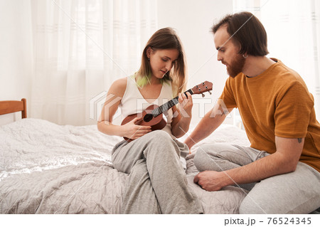 Couple sitting at the sofa and learning how to play at the ukulele 76524345