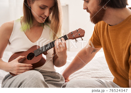 Tender young man helping to his girlfriend with playing at the ukulele 76524347