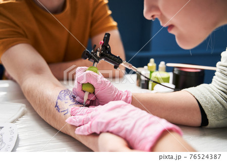 Woman making tattoo for her boyfriend at home with a rotary tattoo machine 76524387