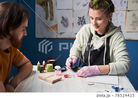 Girl sitting at the table with her boyfriend and preparing to the tattoo session Girl sitting at the table with her boyfriend and preparing to the tattoo session 76524415