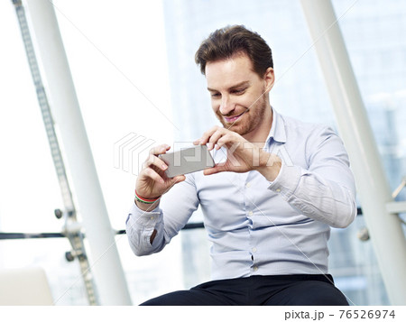 young caucasian business man taking a picture with mobile phone and smiling young caucasian business man taking a picture with mobile phone and smiling 76526974
