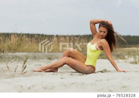 Sensual young woman in bright bodysuit lying on sand 76528328