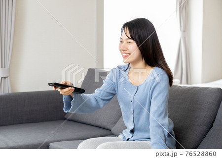 ソファーでリモコンを操作する若い女性 76528860