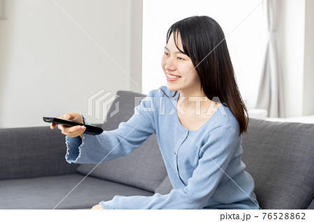 ソファーでリモコンを操作する若い女性 76528862