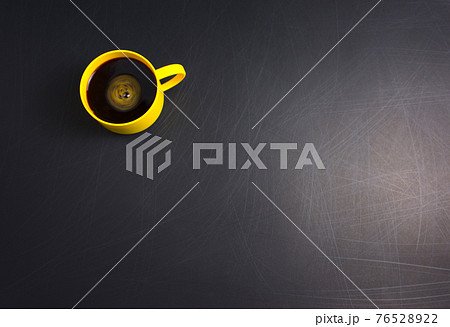 Yellow cup of black coffee flat lay on scratched rough black background. Copy space for your text, image or message. Minimal, top view, horizontal image style. 76528922