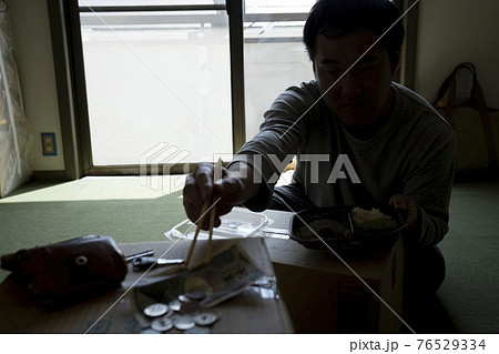 部屋で弁当を食べる男性 76529334
