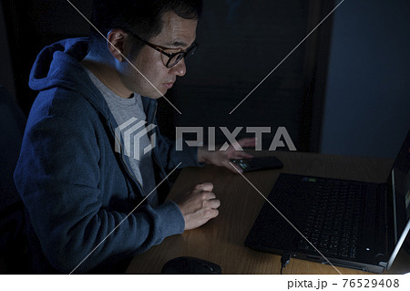 夜にパソコンを見る男性 76529408