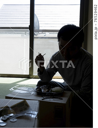 部屋で弁当を食べる男性 76529462