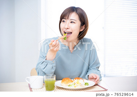 日差しが明るい食卓で朝食を食べる女性 76529614