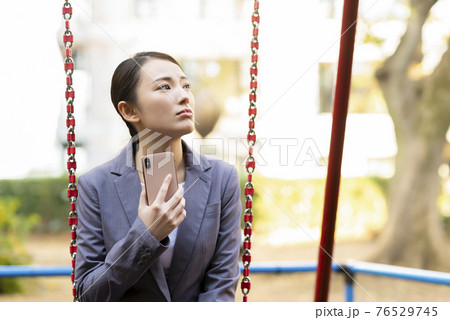 公園でたそがれる若い女性 スーツ スマホ 公園でたそがれる若い女性 スーツ スマホ 76529745