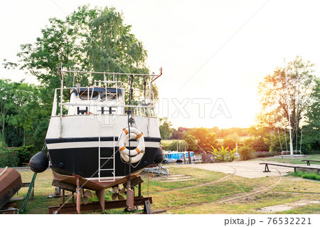 Old motor boat with two lifebuoys is moored in an outdoor workshop under repair 76532221