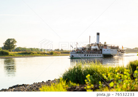 Large retro tourist steamer with a pipe sails along the calm Elbe river 76532233