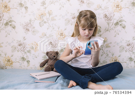 Girl sits on bed, holding phone and reads something in smartphone 76534394