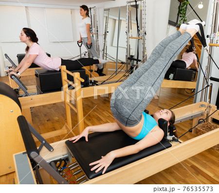 Woman exercising torson rotation at gym using pilates beds 76535573