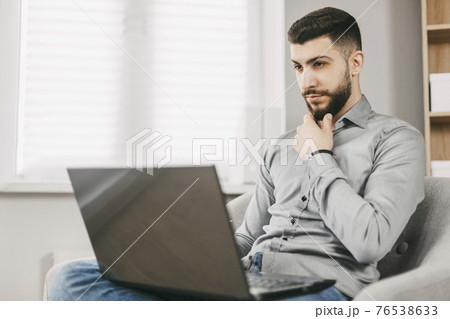 A handsome young man of oriental appearance works at home with a laptop. Doing homework online. Distance learning A handsome young man of oriental appearance works at home with a laptop. Doing homework online. Distance learning 76538633