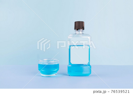 Bottle and glass of mouthwash for oral hygiene routine on light blue background. Mouth rinse liquids help to against bad breath, cavities and plaque. Dental care product. Bottle and glass of mouthwash for oral hygiene routine on light blue background. Mouth rinse liquids help to against bad breath, cavities and plaque. Dental care product. 76539521