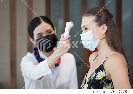Happy guest checking fever by digital thermometer for scan and protect from Coronavirus COVID-19 at hotel reception. 76539706