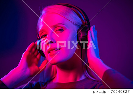 Fashion pretty woman with headphones listening to music over red neon background at studio Fashion pretty woman with headphones listening to music over red neon background at studio 76540327