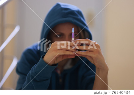 Woman drug addict sits on stairs with syringe Woman drug addict sits on stairs with syringe 76540434