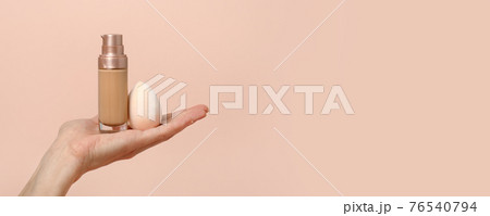 Applying foundation on makeup sponge. Woman's hands with neutral manicure holding bottle of concealer or toner foundation, cream and beauty blender, make up artist background, banner, flyer 76540794