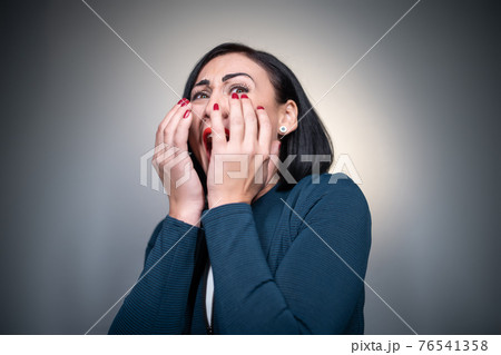 studio shot of scared or afraid brunette female on grey background 76541358