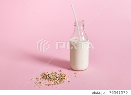 Close-up view of glass bottle with milk and oat flakes on pink background with space for text 76541579