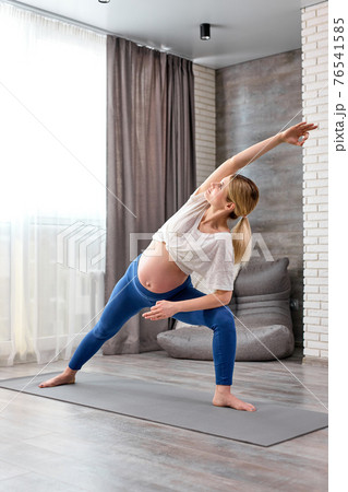 Sporty beautiful pregnant blond woman doing lunge exercise, standing in Extended Side Angle posture at home Sporty beautiful pregnant blond woman doing lunge exercise, standing in Extended Side Angle posture at home 76541585