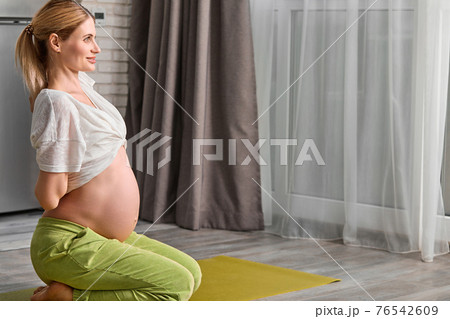 side view on pregnant woman stretching body at home, going to do yoga exercises on floor side view on pregnant woman stretching body at home, going to do yoga exercises on floor 76542609