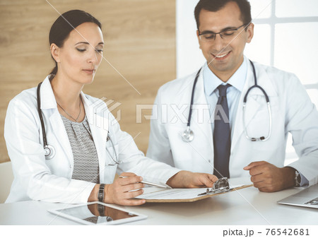 Two doctors discussing treatment problems while sitting at the desk in hospital office. Data in medicine and health care concept 76542681