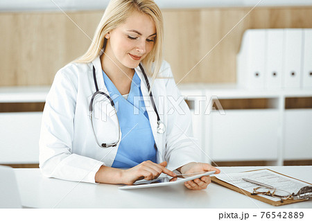 Woman-doctor standing in hospital or clinic and using tablet pc. Data and best service in medicine and healthcare Woman-doctor standing in hospital or clinic and using tablet pc. Data and best service in medicine and healthcare 76542889