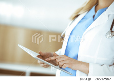 Unknown woman-doctor standing in clinic and using tablet pc, close-up. Data in medicine and healthcare Unknown woman-doctor standing in clinic and using tablet pc, close-up. Data in medicine and healthcare 76542902