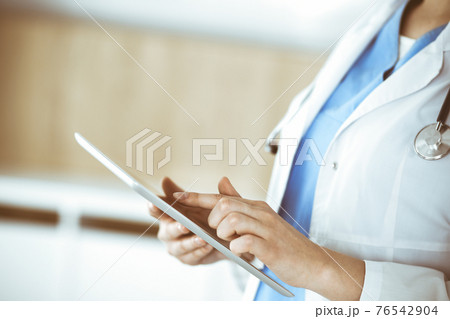 Unknown woman-doctor standing in clinic and using tablet pc, close-up. Data in medicine and healthcare 76542904