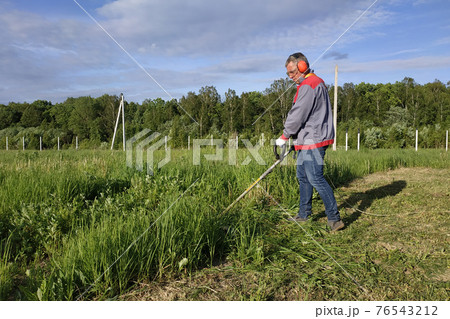 Man mows the grass with a trimmer, tall grass in a meadow, handmade in the garden. 76543212
