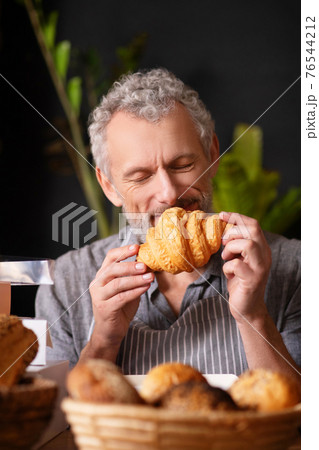 Man with closed eyes inhaling smell of croissant 76544212