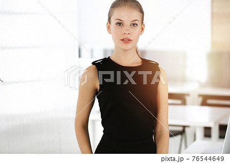Young blond businesswoman dressed in black dress looks perfect in sunny modern office. Business people concept 76544649