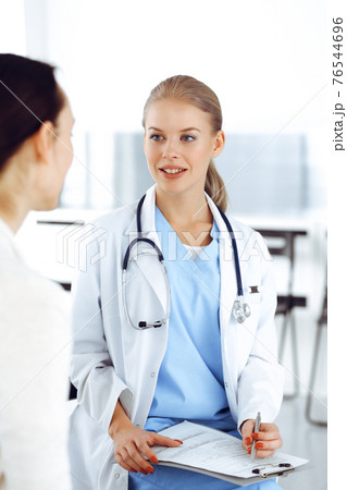 Woman - doctor consults her female patient while using clipboard and medication history record. Medicine concept 76544696