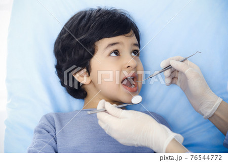 Cute arab boy sitting at dental chair with open mouth during oral checking up with doctor. Visiting dentist office. Stomatology concept Cute arab boy sitting at dental chair with open mouth during oral checking up with doctor. Visiting dentist office. Stomatology concept 76544772