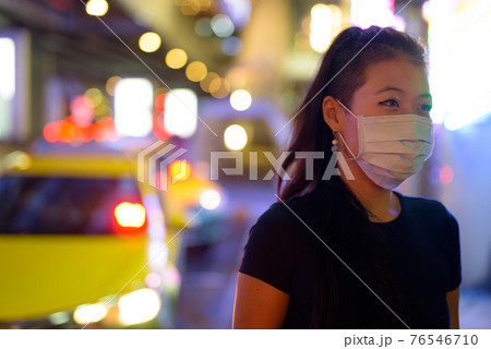Asian woman wearing face mask to protect from covid 19 outdoors at night while at taxi station Asian woman wearing face mask to protect from covid 19 outdoors at night while at taxi station 76546710
