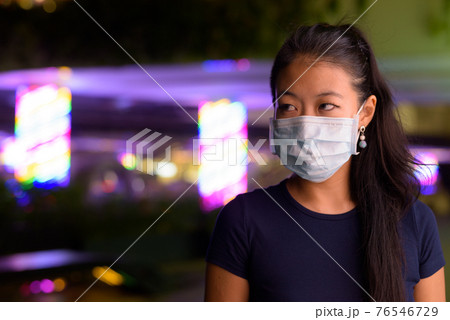 Asian woman thinking and wearing face mask to protect from covid 19 outdoors at night 76546729