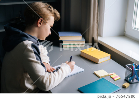 High-angle view of back view of pupil boy reading paper study book sitting at desk near window in children room.  76547880