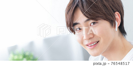 自宅のリビングでスマホを手にする若い男性　バナーサイズ 76548517