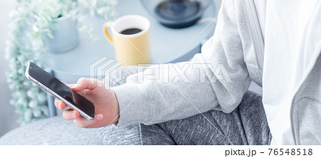 自宅のリビングでスマホを手にする若い男性の手元　バナーサイズ 76548518