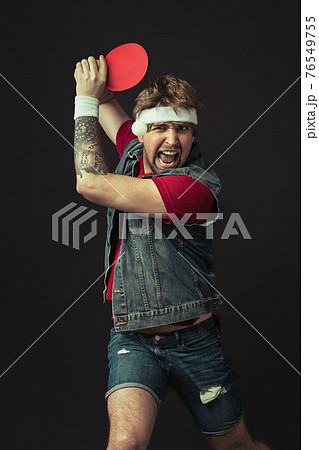 Young Caucasian funny man playing ping pong isolated on black background. Young Caucasian funny man playing ping pong isolated on black background. 76549755