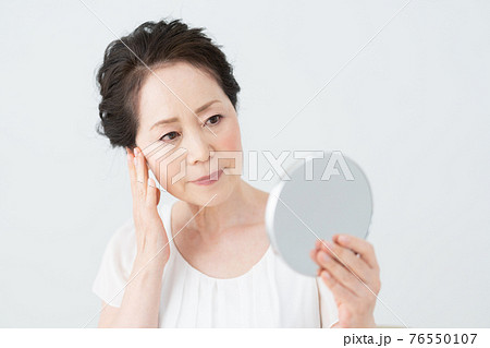 鏡を見て目尻の皺をチェックするシニア女性 76550107