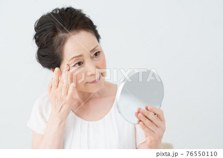 鏡を見て目尻の皺をチェックするシニア女性 76550110