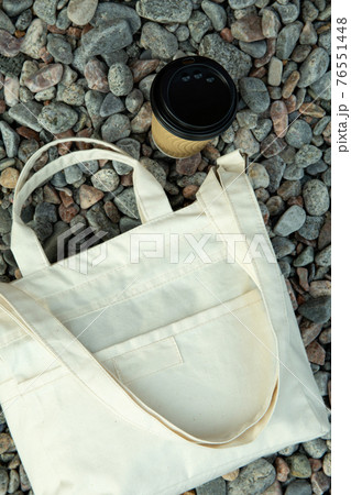 Stylish eco bag and paper cup outdoor on pebbles 76551448