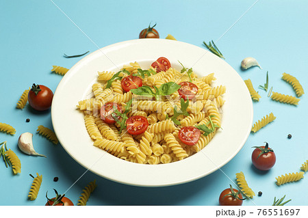 Food pasta on a blue background. Italian fusilli pasta with tomatoes, herbs and basil on a white plate. Healthy food concept. Food pasta on a blue background. Italian fusilli pasta with tomatoes, herbs and basil on a white plate. Healthy food concept. 76551697