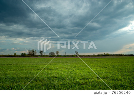 Green field and dark storm clouds on the sky Green field and dark storm clouds on the sky 76556240