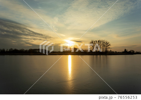Sunset over a frozen lake with trees on the shore Sunset over a frozen lake with trees on the shore 76556253